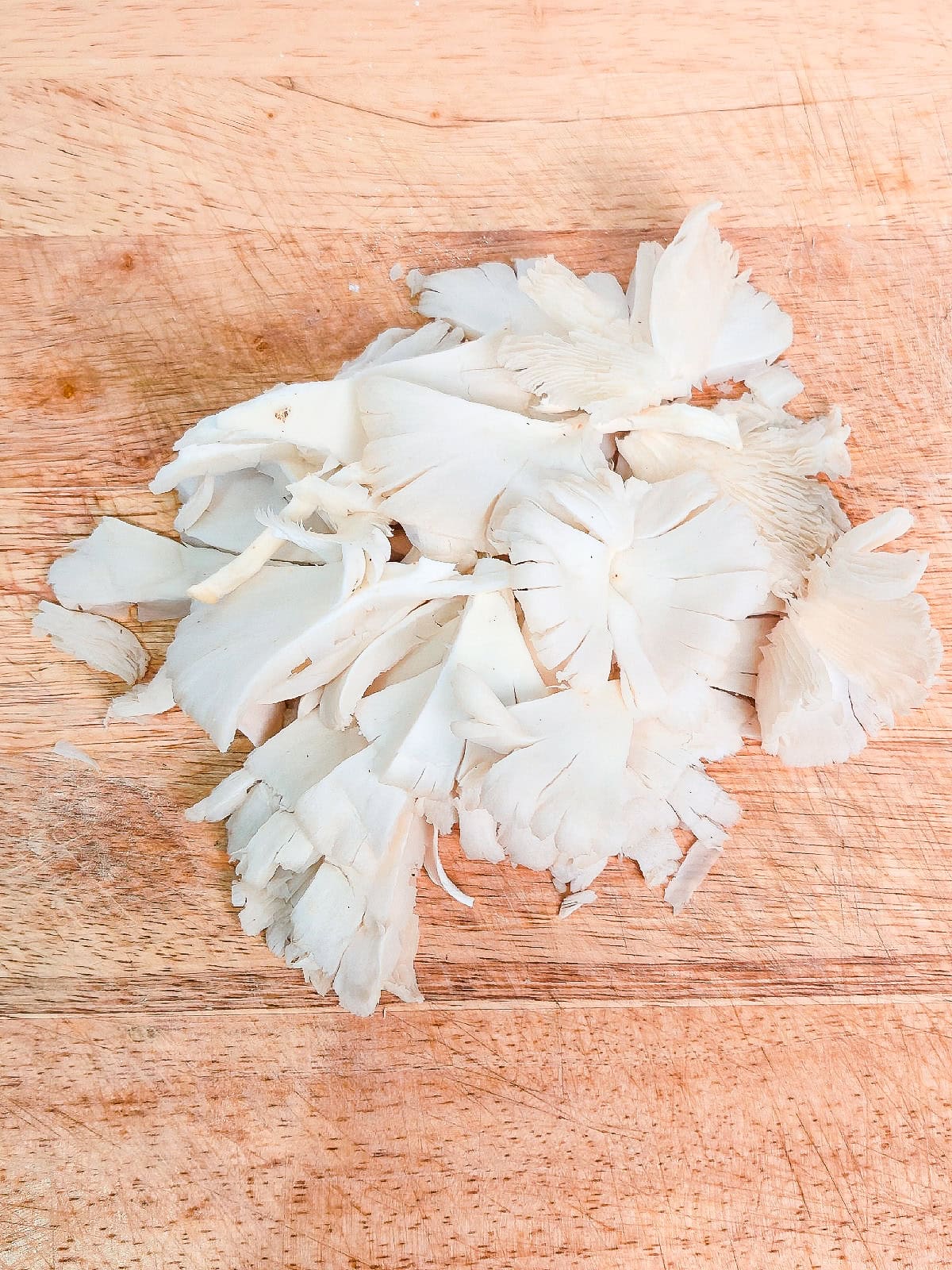 Fresh oyster mushrooms torn into bite-sized pieces on a wooden cutting board.