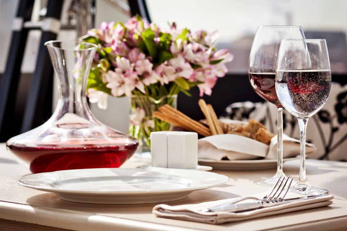 Elegant table setting with wine glasses, a decanter of red wine, bread, and a floral centerpiece.