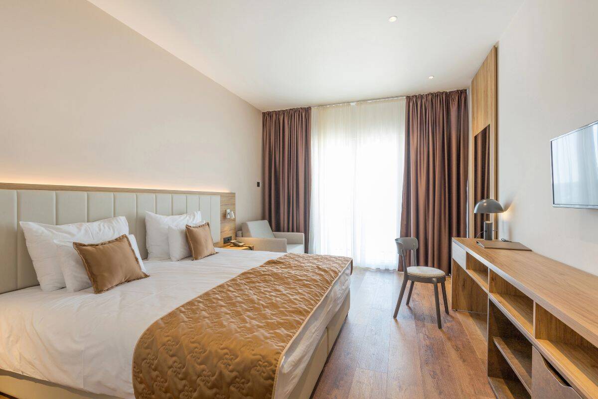 A modern hotel-style bedroom with a neatly made bed, wooden desk, and soft neutral decor.