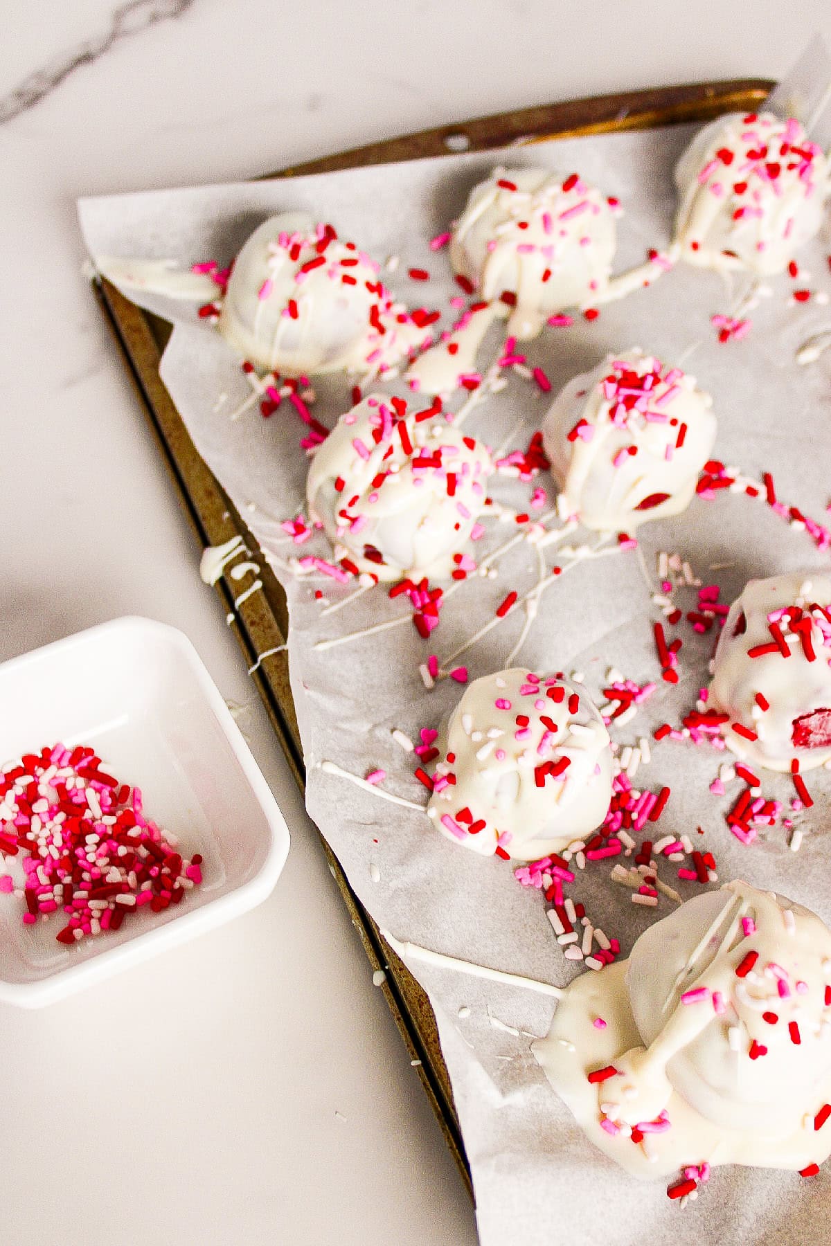 Red velvet truffles coated in white chocolate and topped with pink and red sprinkles on a white plate.
