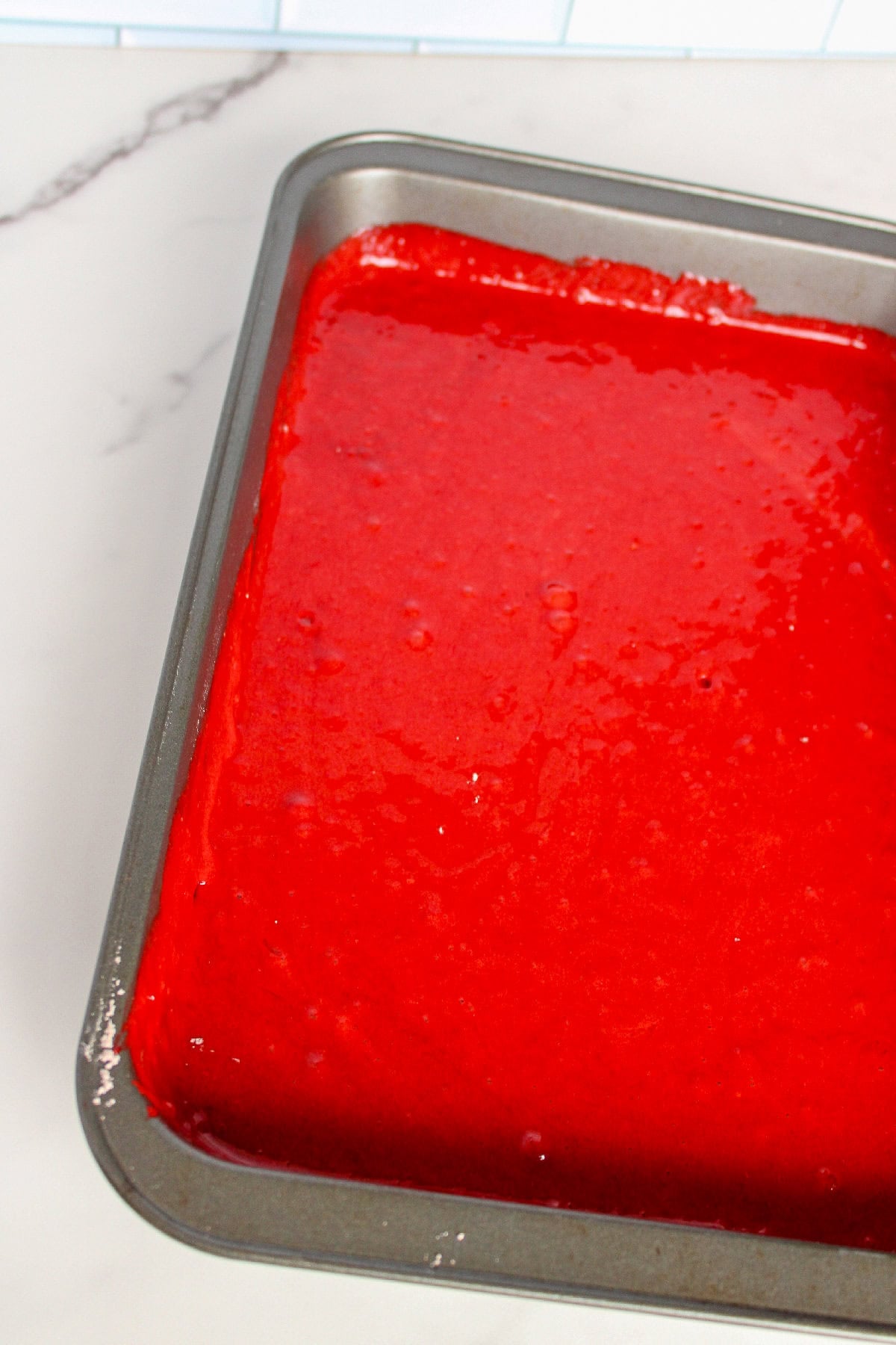 Unbaked red velvet cake batter spread evenly in a rectangular baking pan.