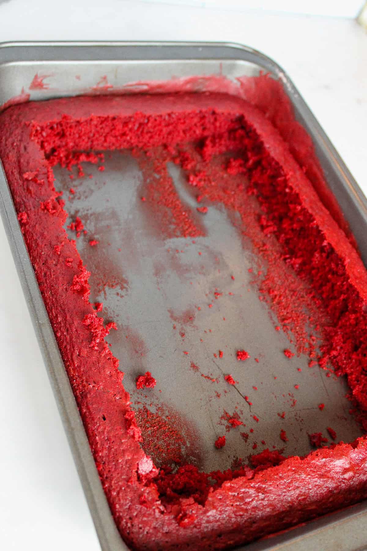 Red velvet cake with edges removed and crumbled inside the baking pan.