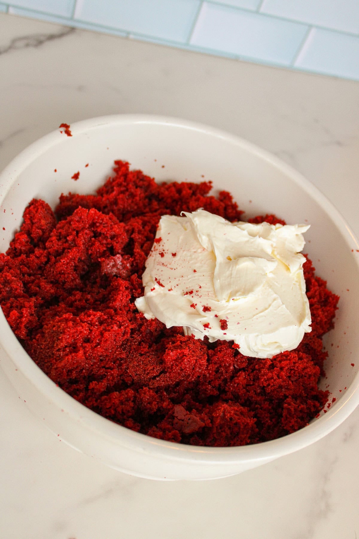 Crumbled red velvet cake mixed with softened cream cheese in a white bowl.