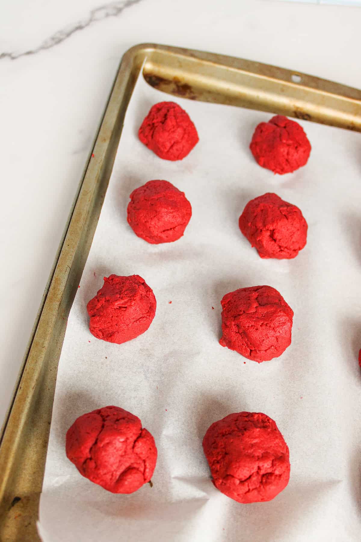 Rolled red velvet cake balls arranged on a parchment-lined baking sheet.