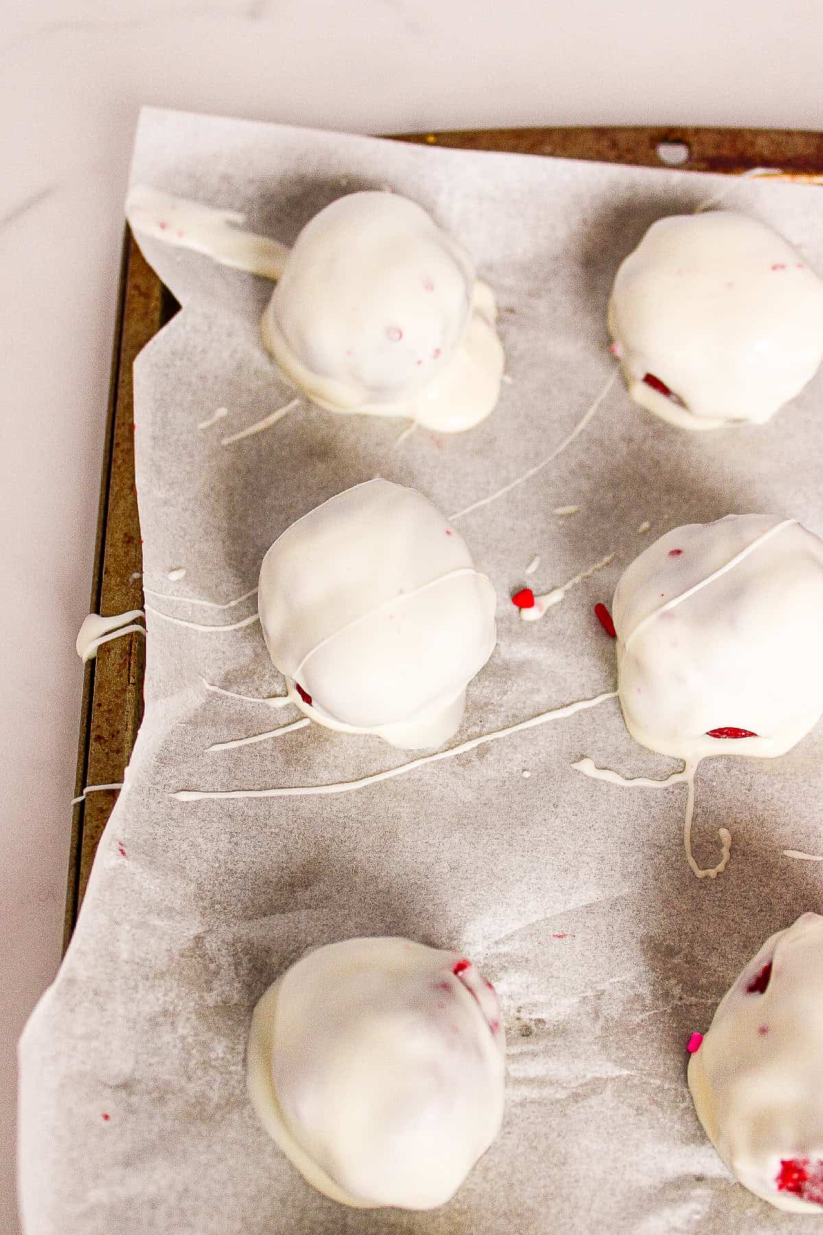 White chocolate-coated red velvet truffles setting on parchment paper.