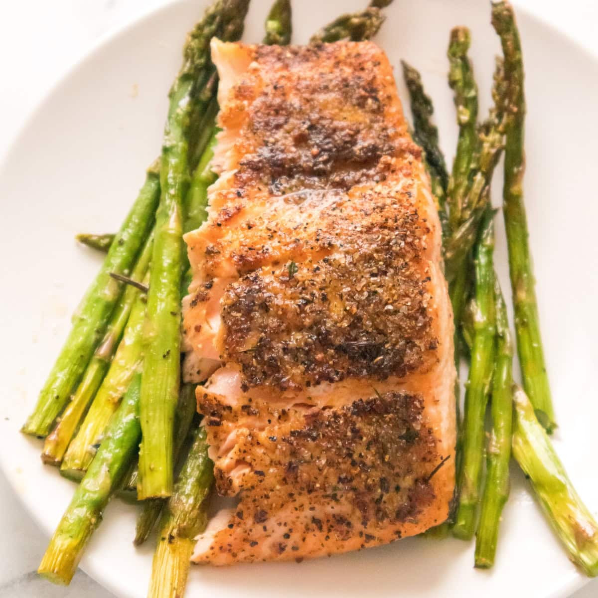 Air fryer salmon fillet with crispy seasoning served over roasted asparagus on a white plate.