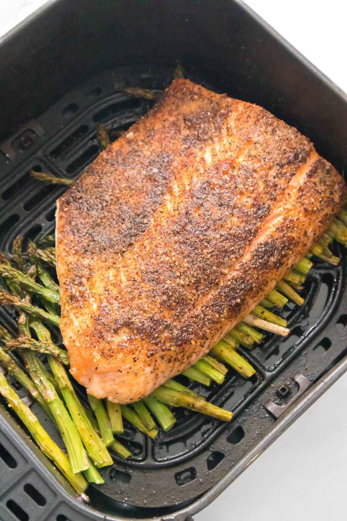 Air fryer salmon and asparagus cooking in basket with seasoned salmon fillet.