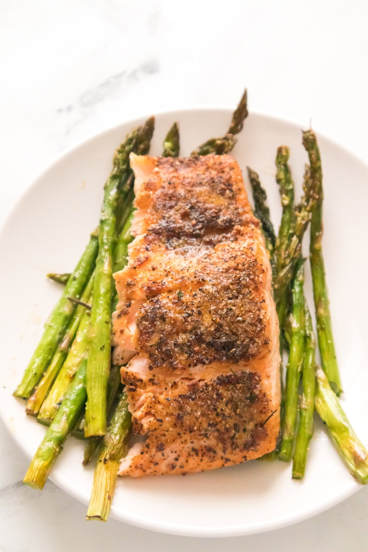 Air fryer salmon and asparagus served on white plate with crispy edges.