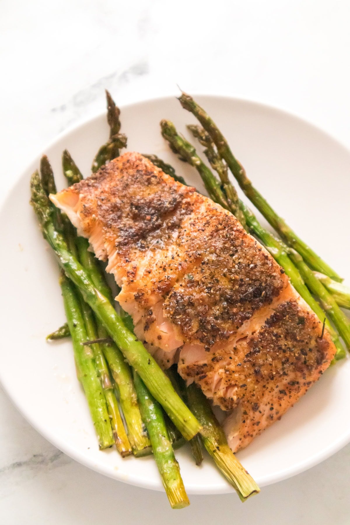 Healthy air fryer salmon with roasted asparagus on white plate.
