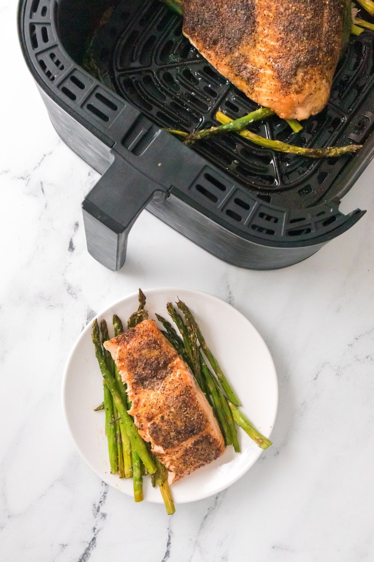 Air fryer salmon and asparagus with cooked fillet in basket and plated serving.