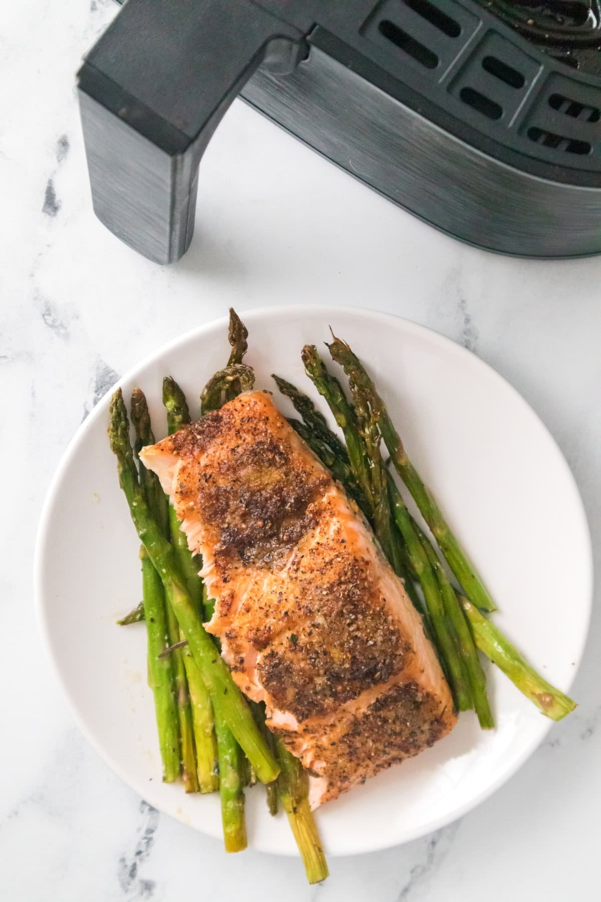 Air fryer salmon and asparagus served on white plate with roasted asparagus.