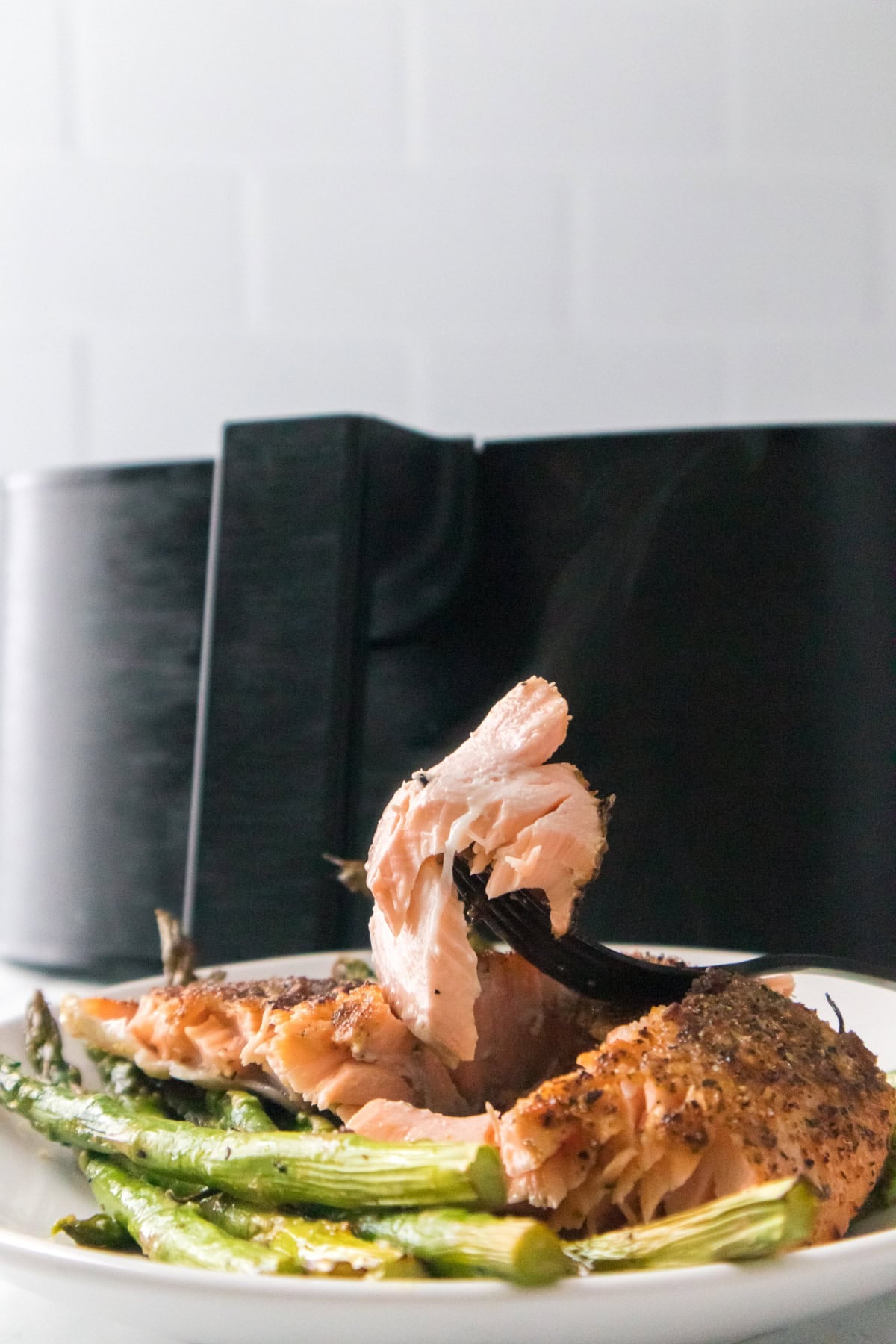 Flaky air fryer salmon being lifted with fork over roasted asparagus.
