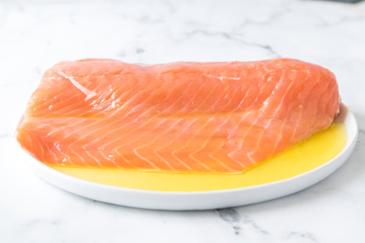 Raw salmon fillet coated with olive oil on a plate ready for air fryer salmon and asparagus recipe.