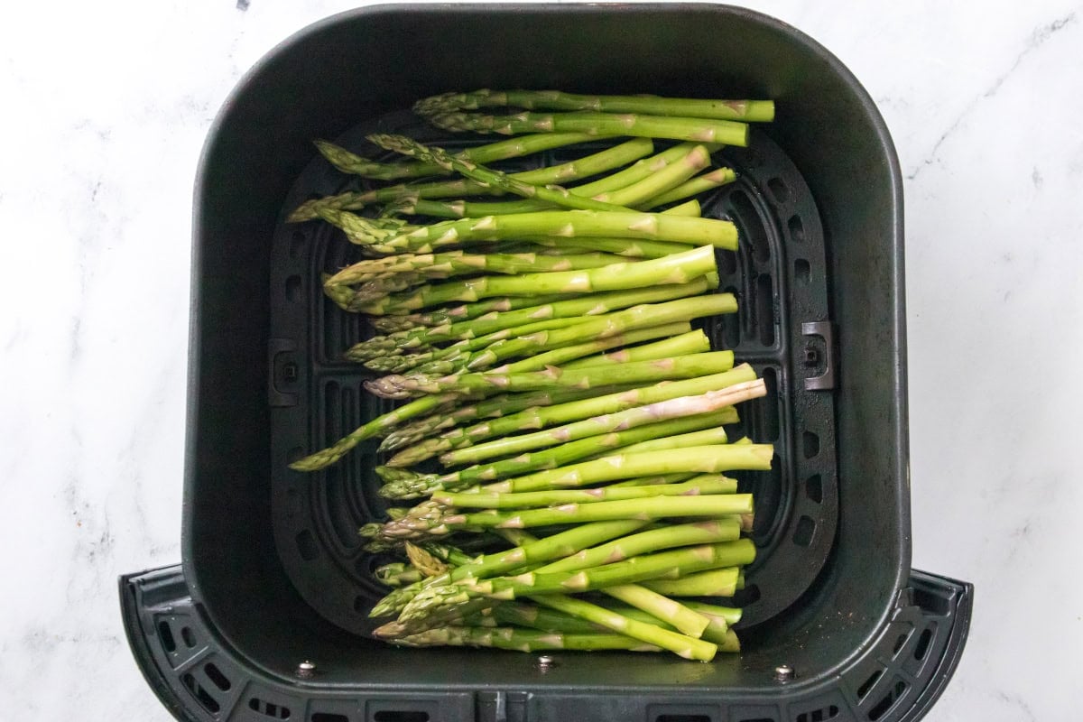Fresh asparagus arranged in an air fryer basket for air fryer salmon and asparagus recipe.
