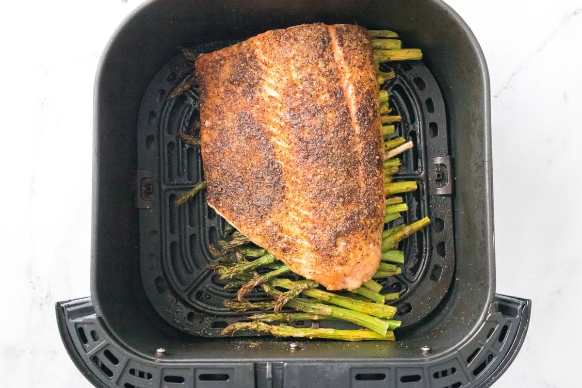 Air fryer salmon and asparagus cooking in air fryer basket with seasoned salmon fillet.
