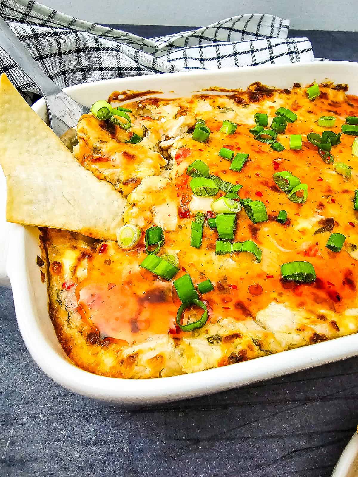 Close-up of hot crab Rangoon dip with crab, cream cheese, green onions, and sweet chili sauce topping.