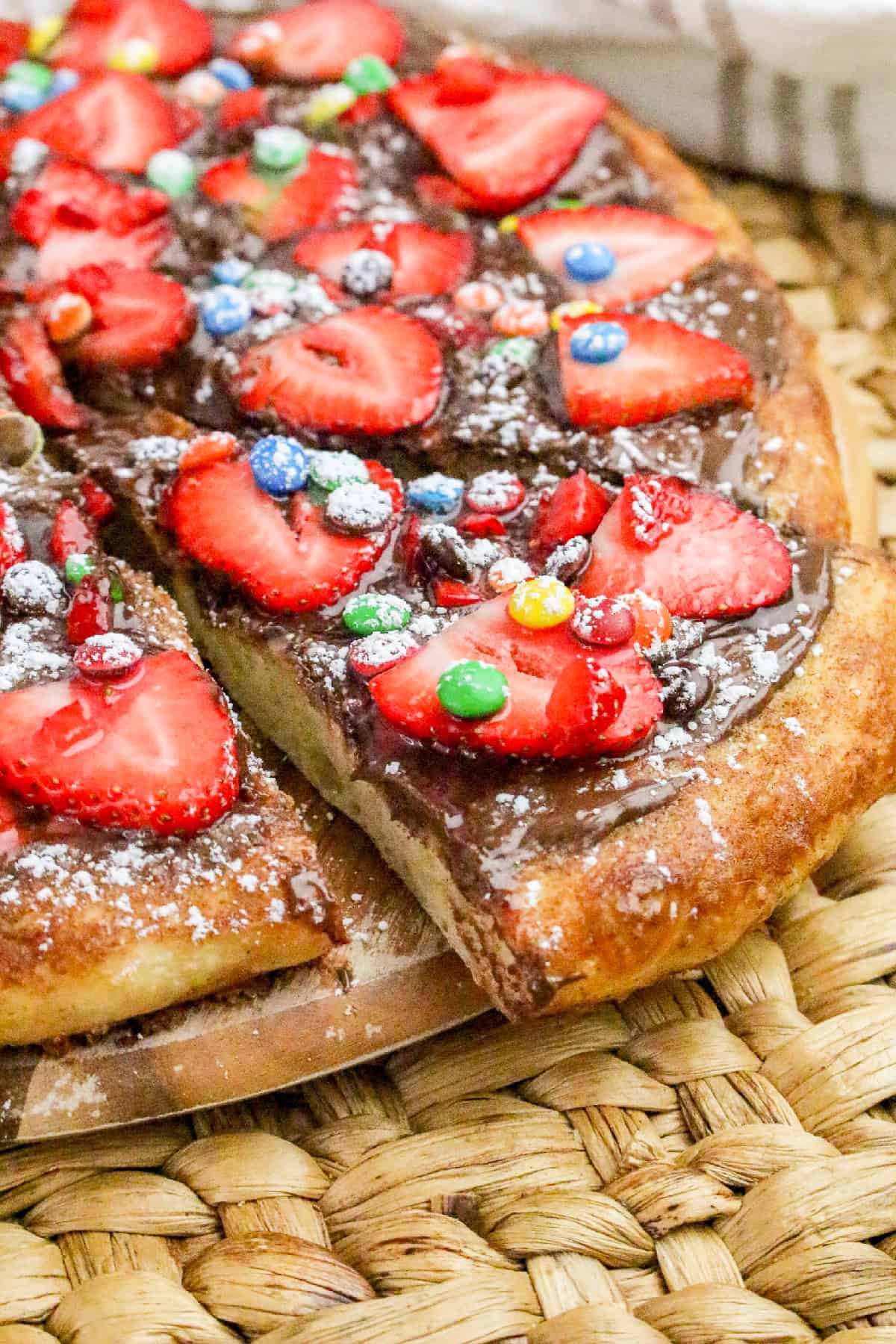 Nutella dessert pizza slices topped with fresh strawberries, colorful candy pieces, and powdered sugar.