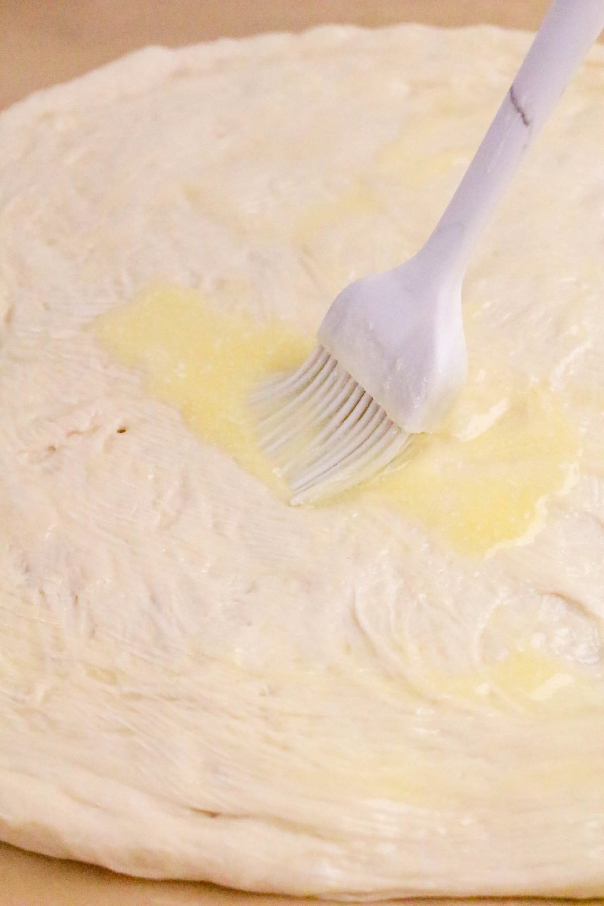 Brushing melted butter onto stretched pizza dough to prepare the base for homemade Nutella dessert pizza.