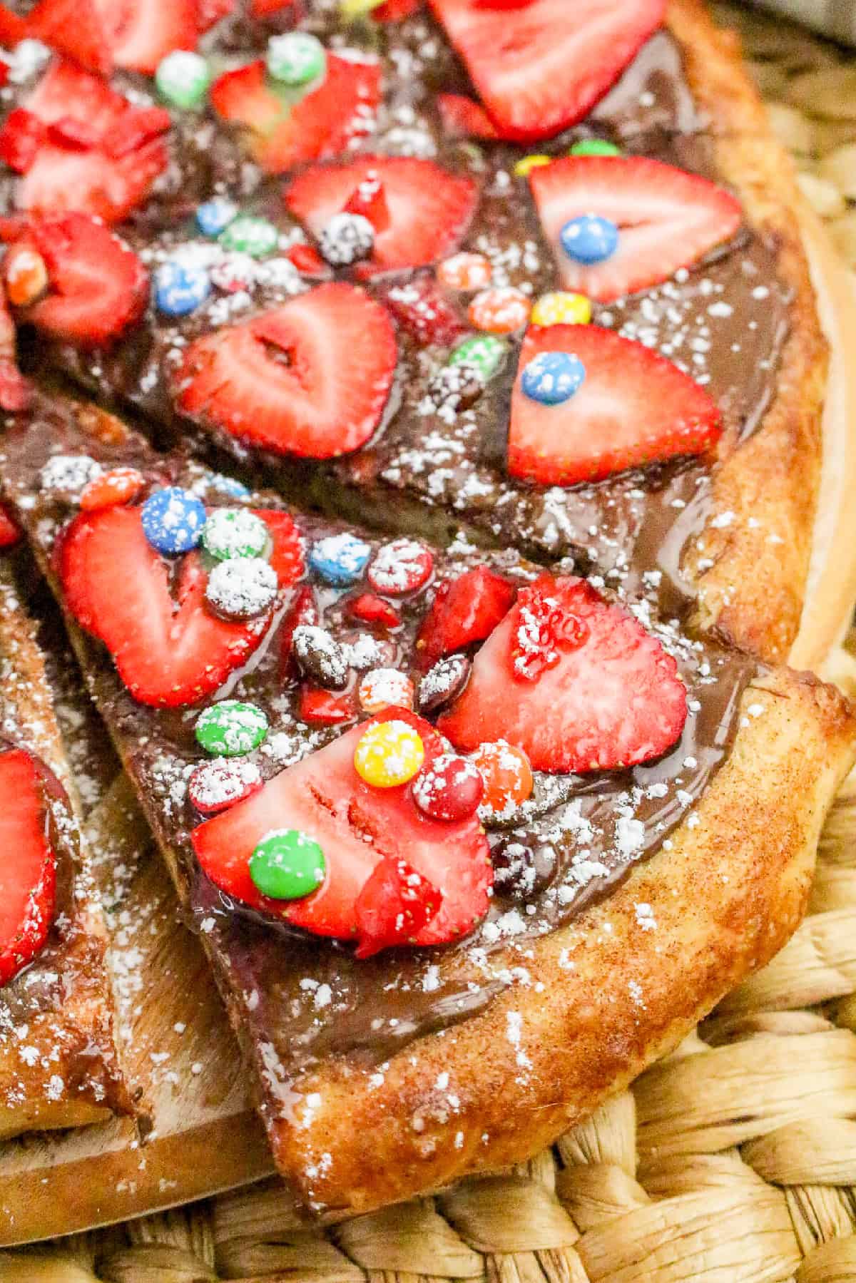 Close-up of homemade Nutella pizza slice with strawberries, candy toppings, and powdered sugar.