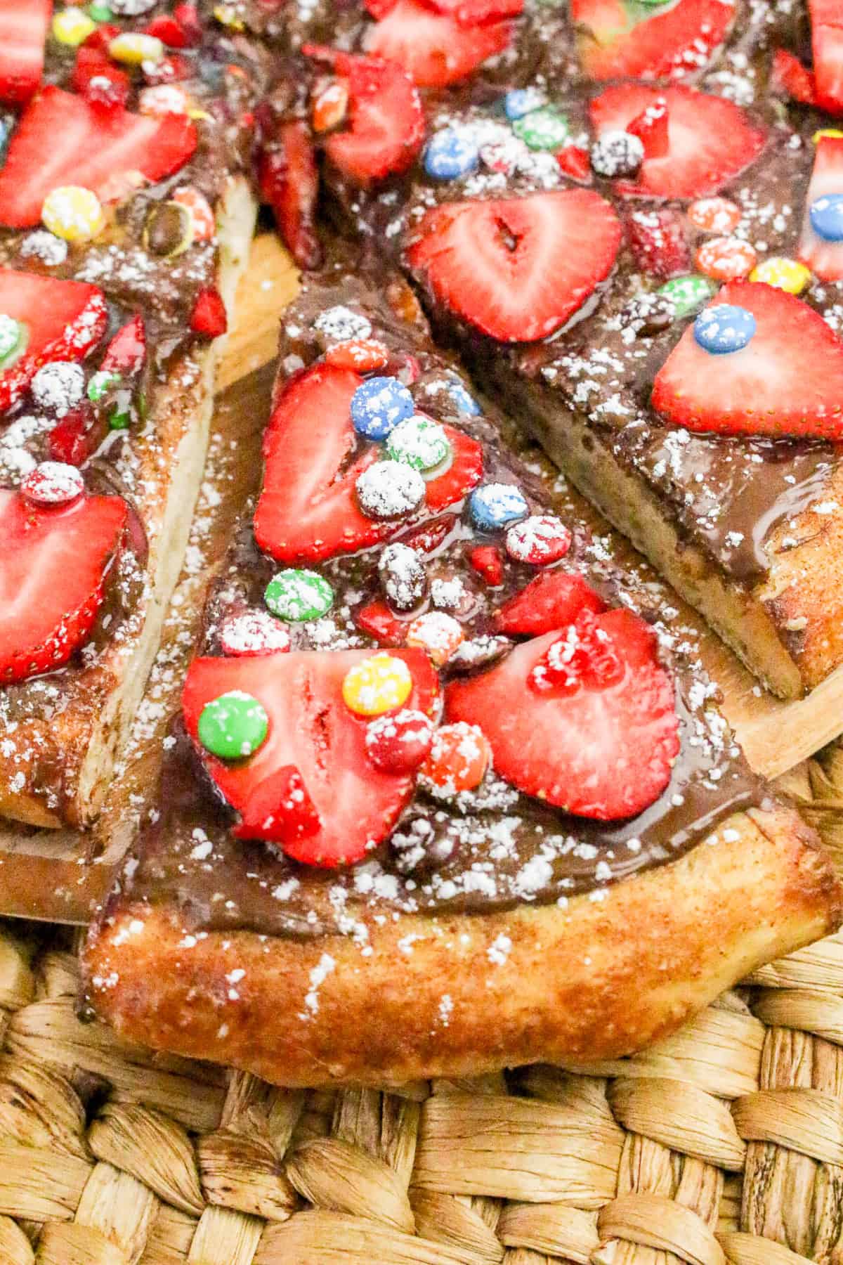 Nutella pizza sliced and served with strawberries, candy toppings, and powdered sugar on sweet pizza crust.