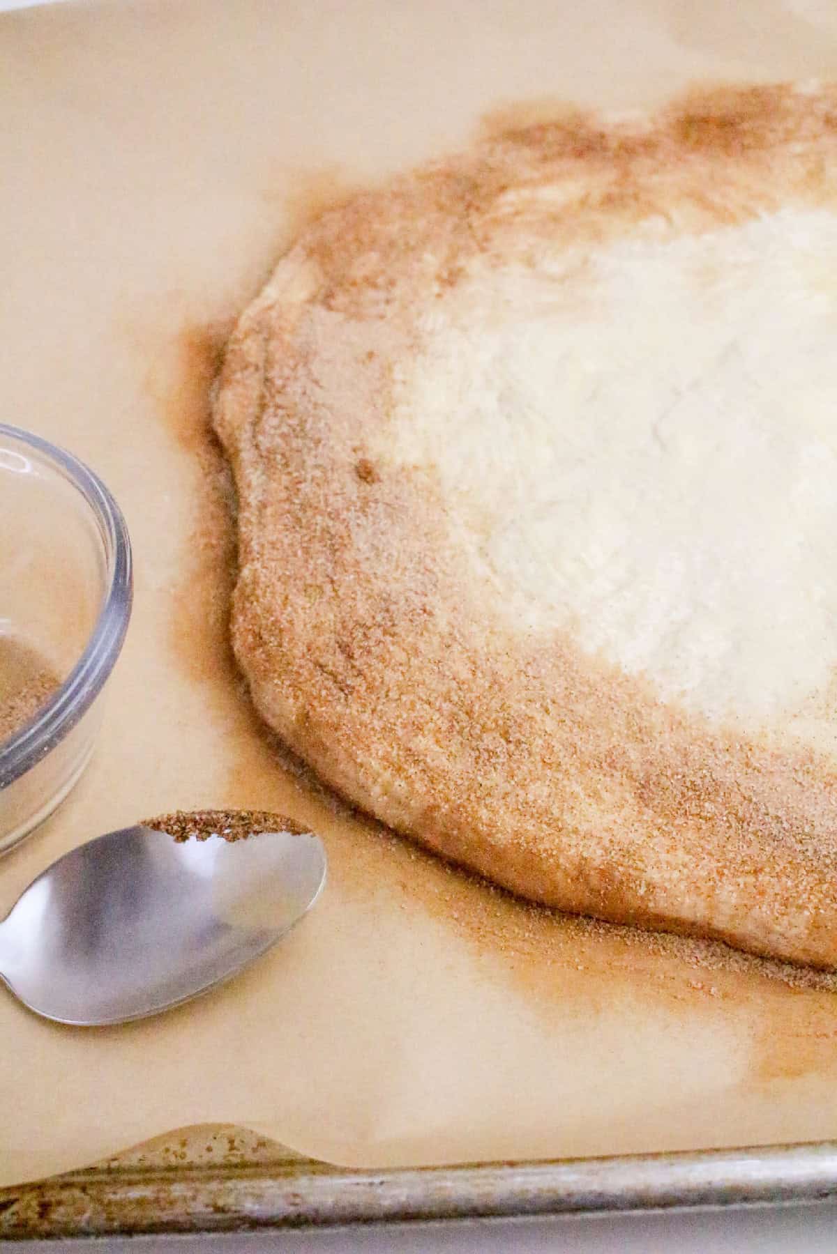 Pizza dough sprinkled with cinnamon sugar on parchment paper to create a sweet crust for Nutella dessert pizza.