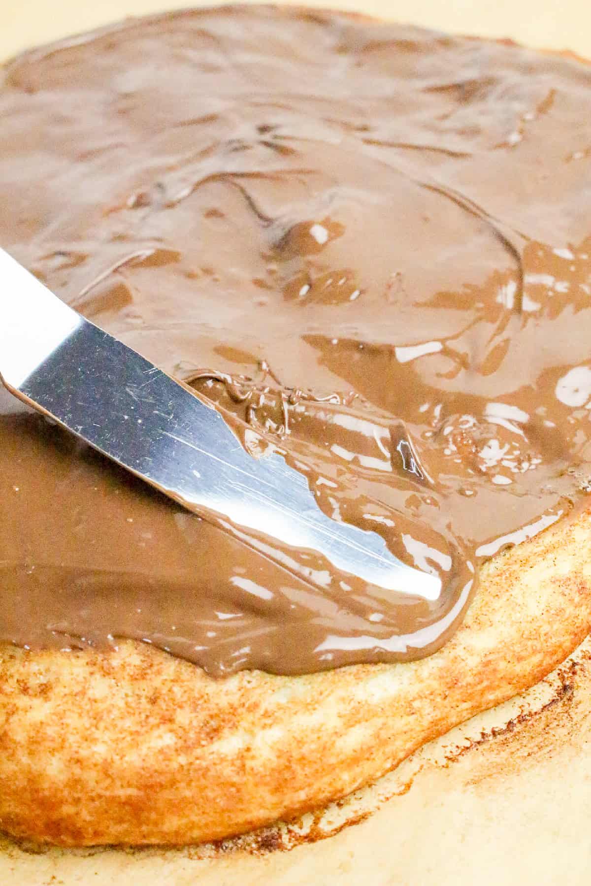 Spreading melted Nutella over warm pizza crust with a knife to make an easy homemade Nutella dessert pizza.