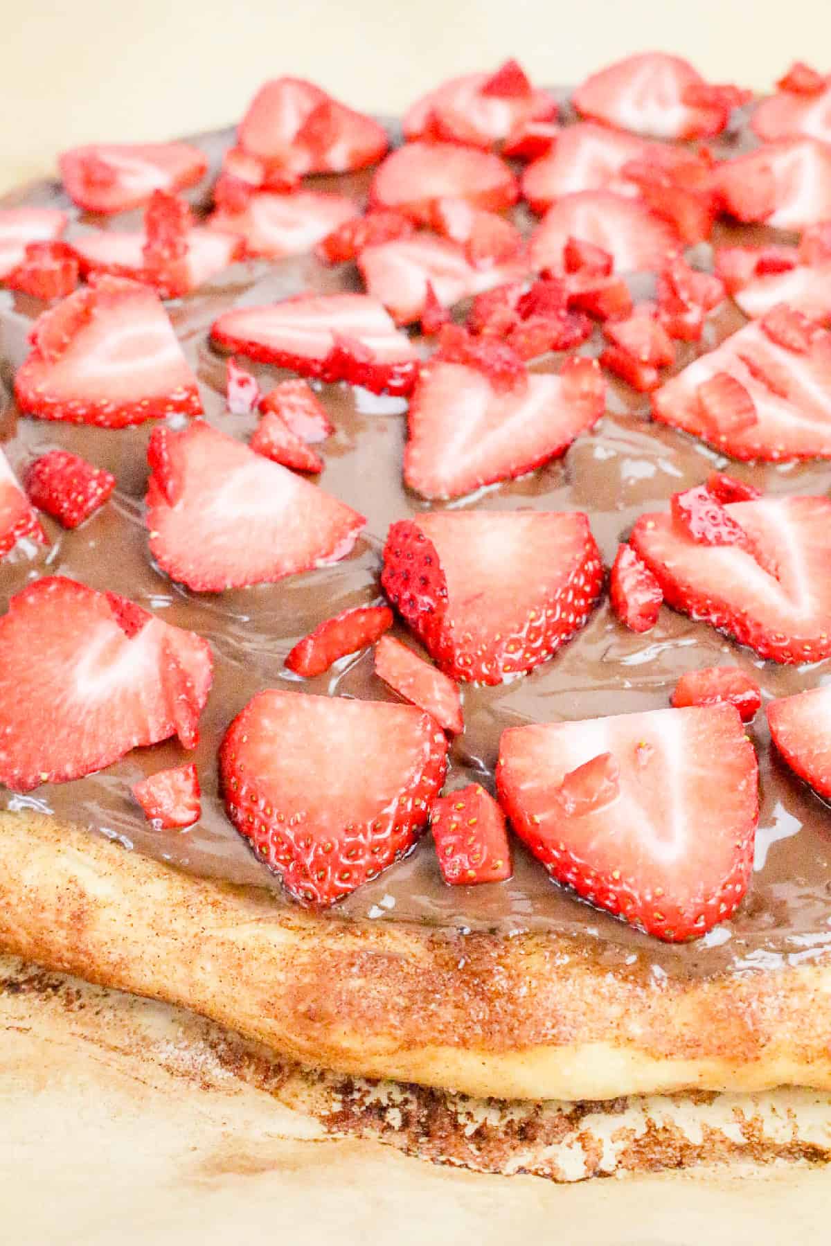 Fresh sliced strawberries scattered over Nutella on baked pizza crust to make a sweet Nutella dessert pizza.