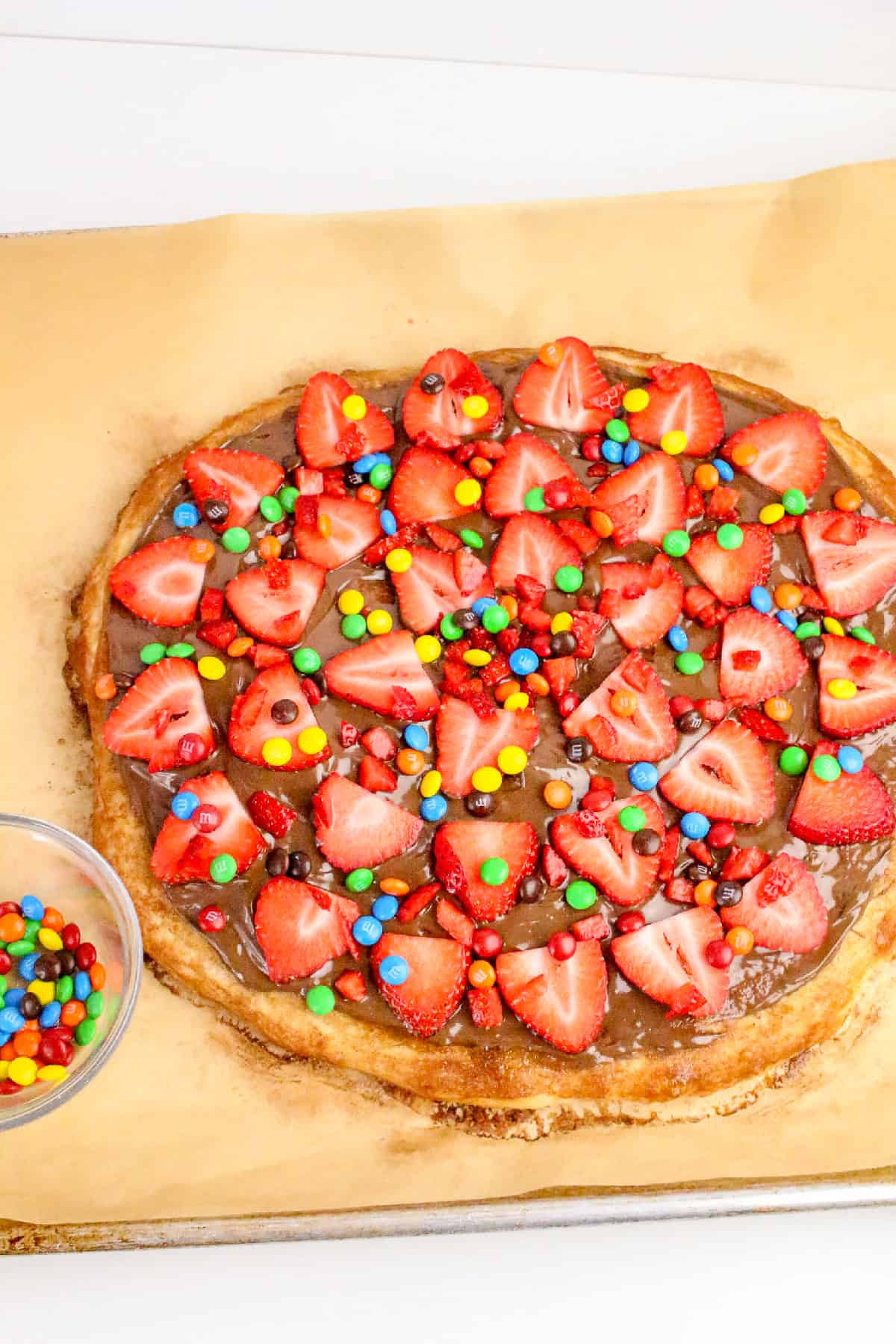 Nutella dessert pizza topped with fresh strawberries and colorful candy pieces on a homemade pizza crust.