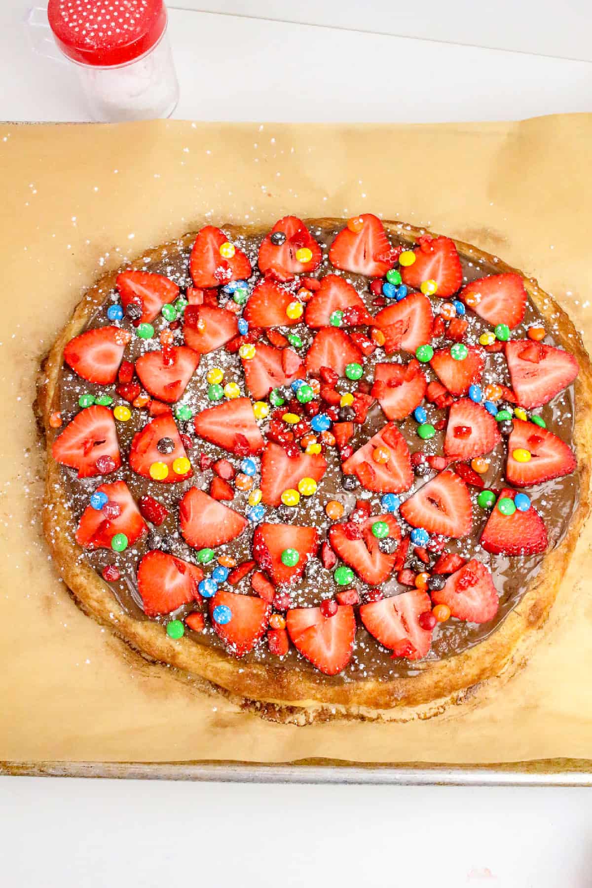 Easy homemade Nutella pizza with strawberries, candy toppings, and powdered sugar on a baked dessert pizza crust.