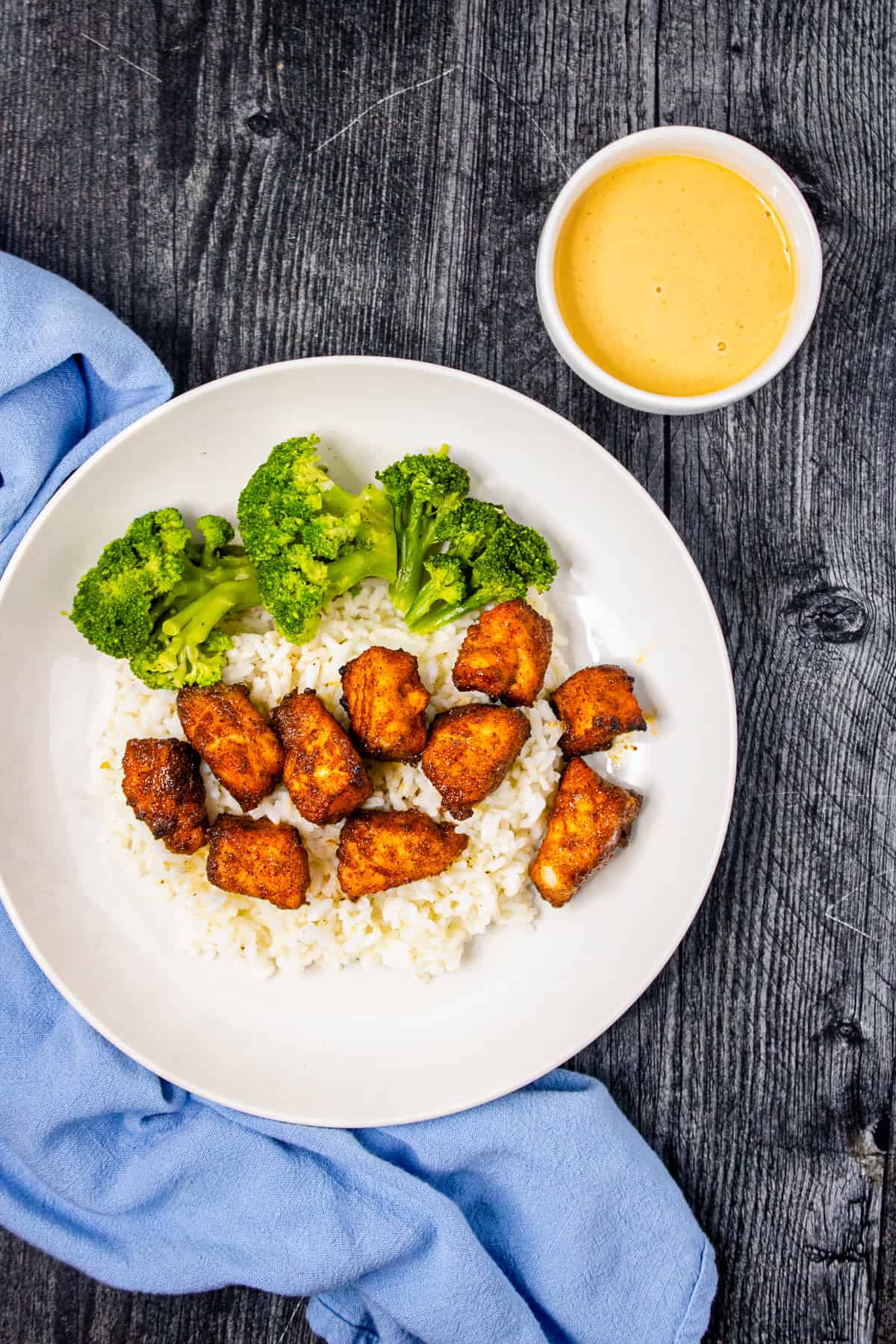 Air fryer salmon bites bowl with rice, broccoli, and dipping sauce on a wooden table.