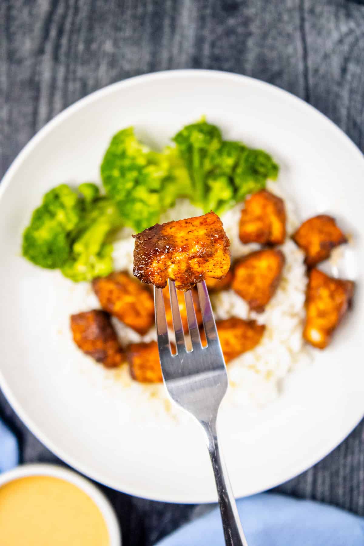 Close-up of a fork holding a crispy air fryer salmon bite above a rice bowl.