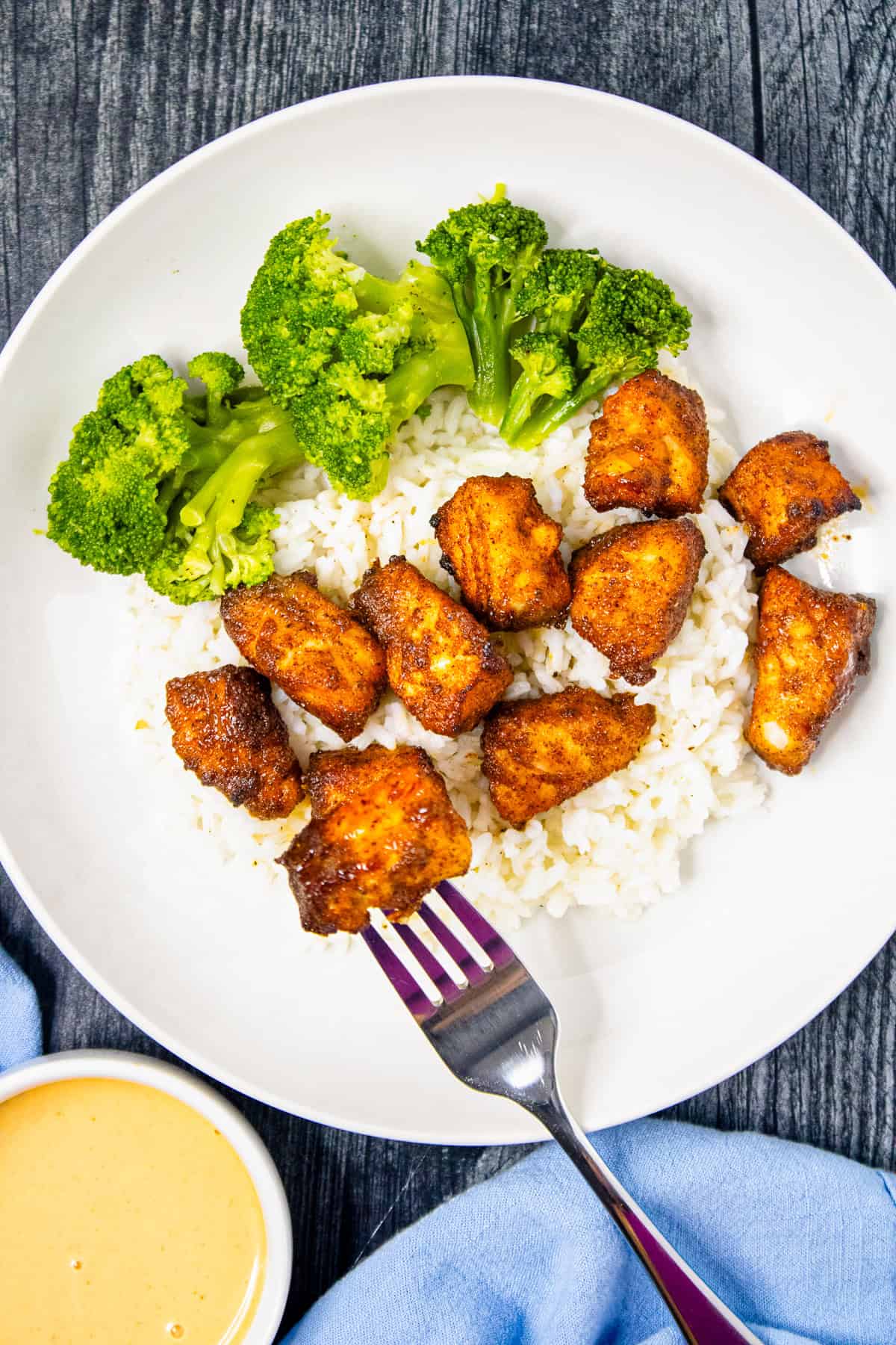Fork lifting an air fryer salmon bite from a bowl with rice and broccoli.
