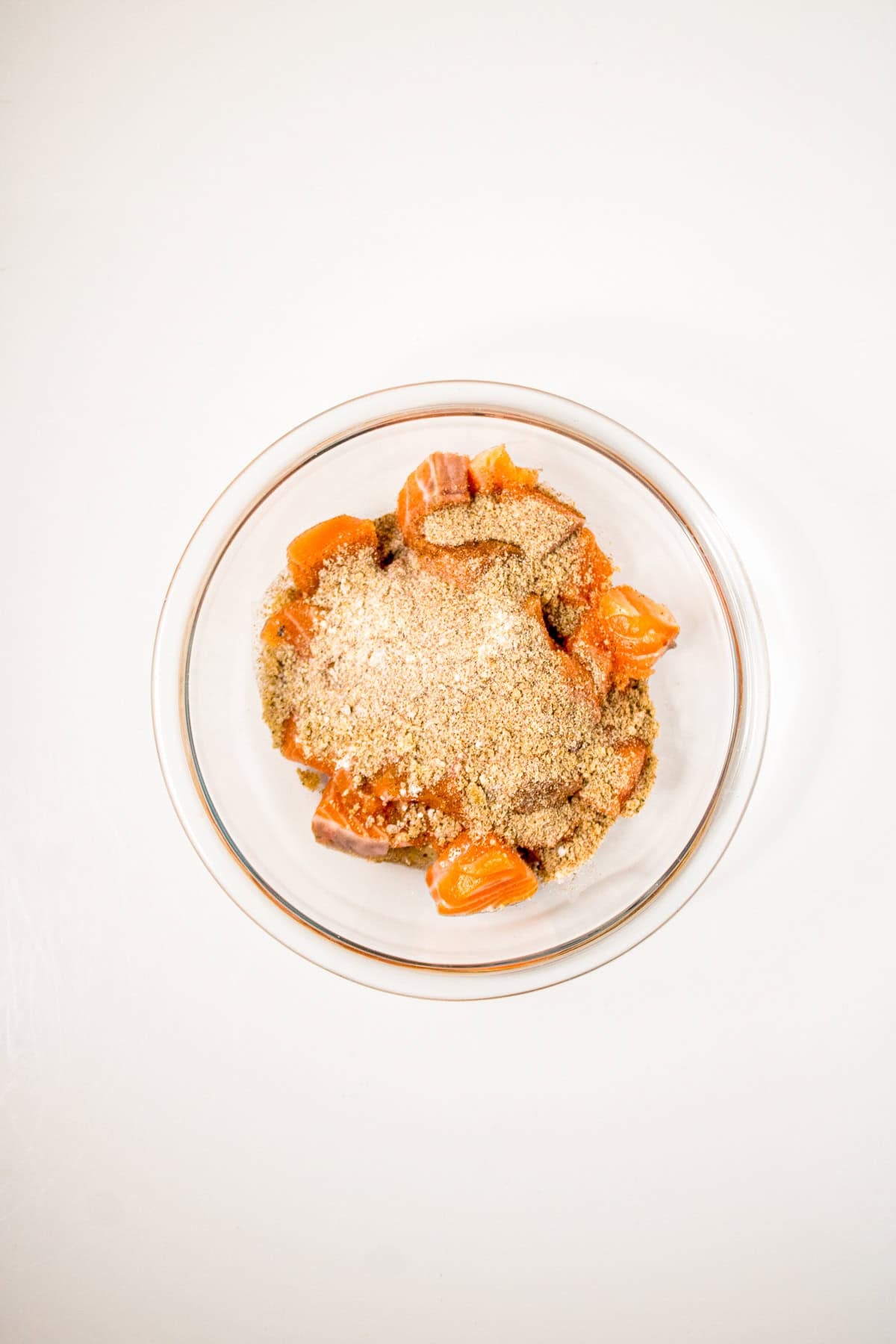 Cubed salmon pieces topped with seasoning mixture in a glass bowl before mixing for air fryer salmon bites.