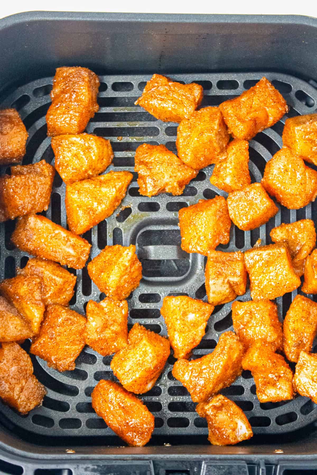 Seasoned salmon bites arranged in an air fryer basket ready to cook.