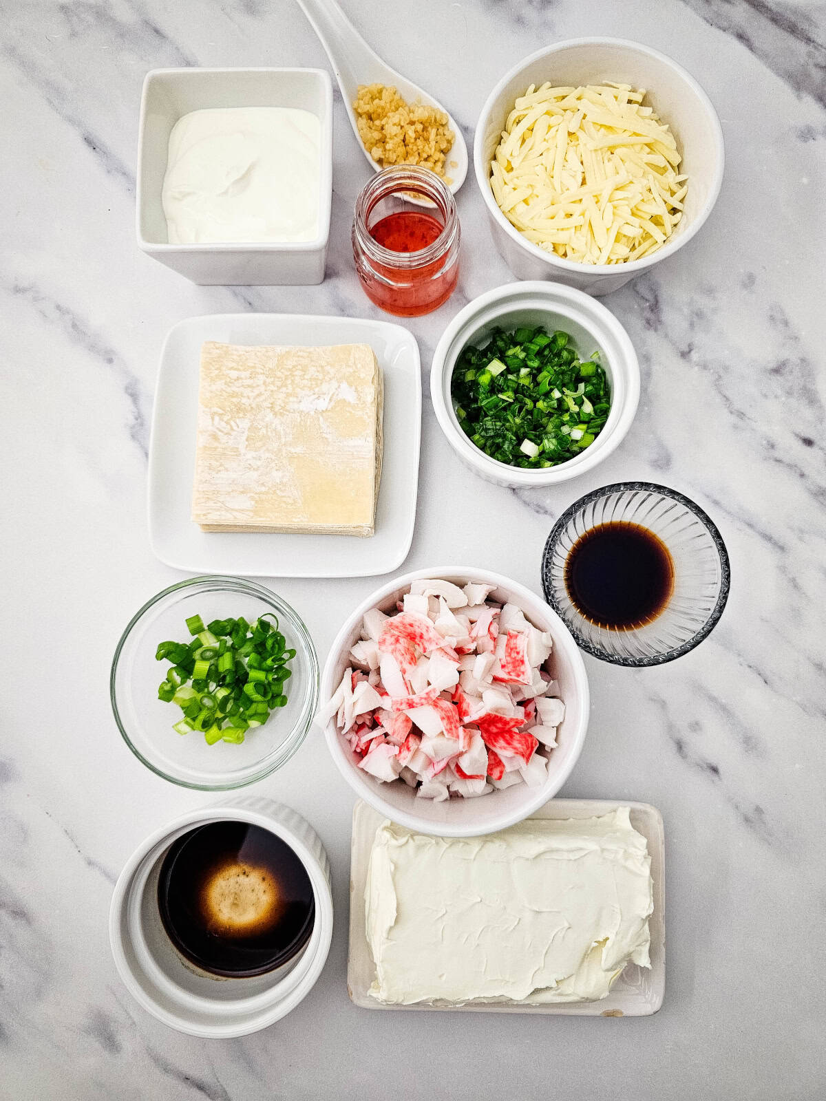 Ingredients for crab Rangoon dip including cream cheese, sour cream, imitation crab, shredded cheese, green onions, jalapeños, sweet chili sauce, soy sauce, and wonton wrappers.