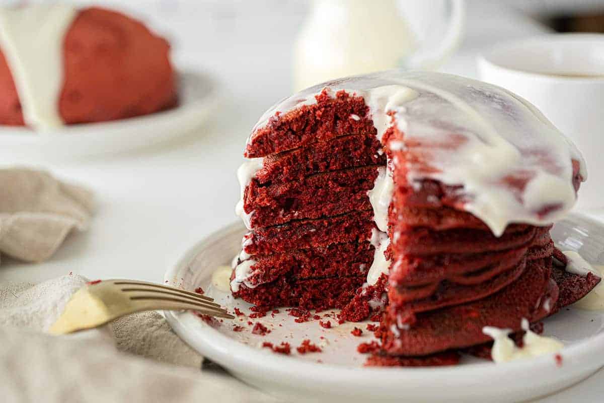 Red velvet cake batter pancakes topped with syrup and cream cheese drizzle.