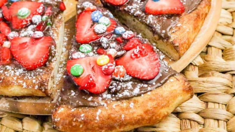 Nutella pizza topped with fresh strawberry slices, colorful candy pieces, and powdered sugar on a cinnamon-sugar crust.