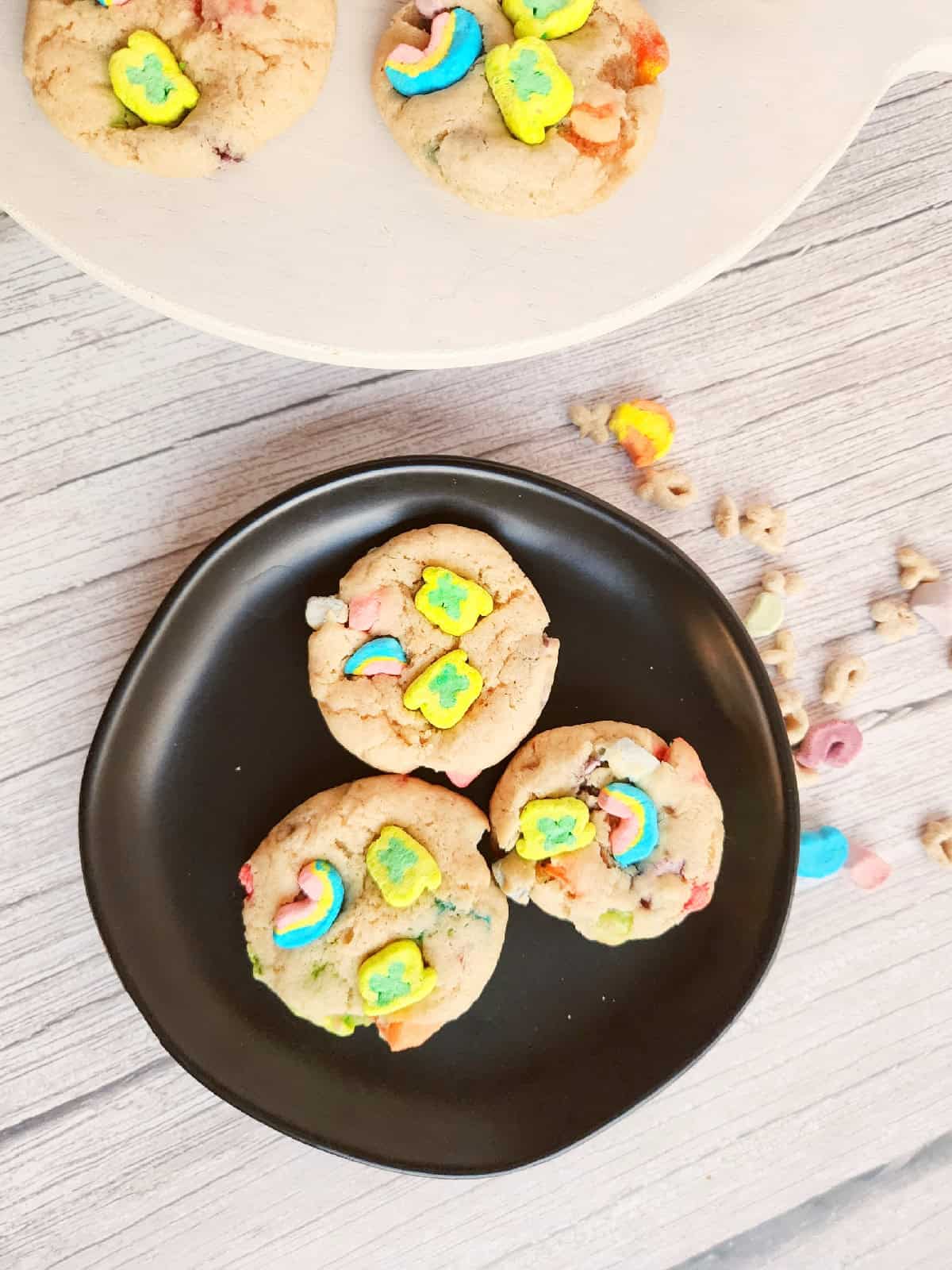 Lucky Charms cookies served on a black plate with colorful cereal marshmallows on top.