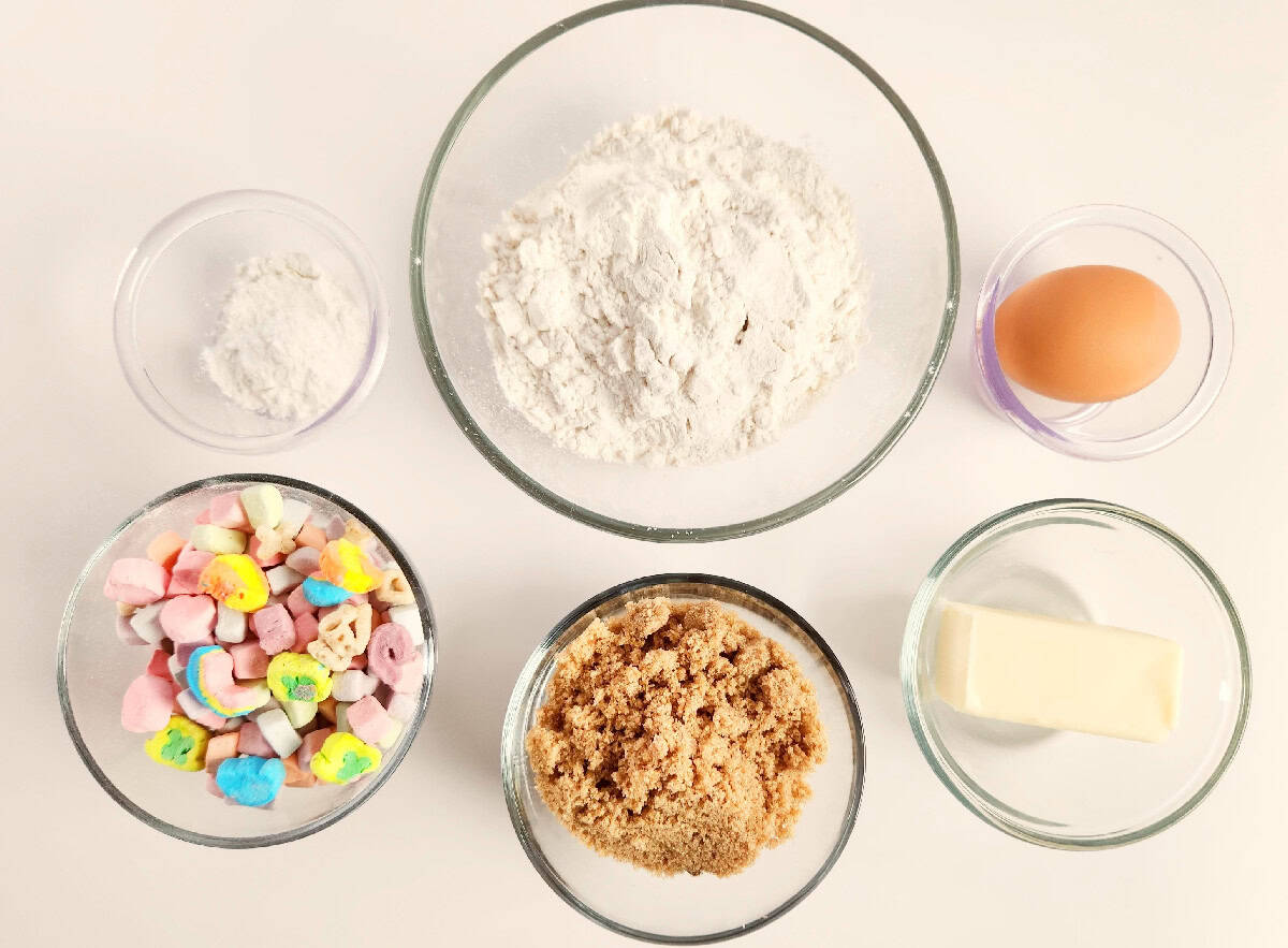 Lucky Charms cookies ingredients, including flour, brown sugar, butter, egg, baking powder, and Lucky Charms marshmallows, in small bowls.