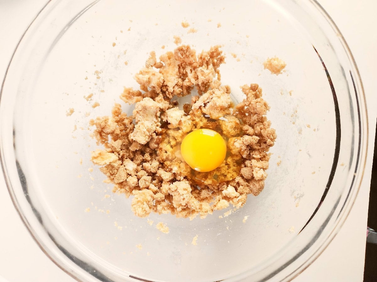 Egg added to the butter and brown sugar mixture in a glass mixing bowl.