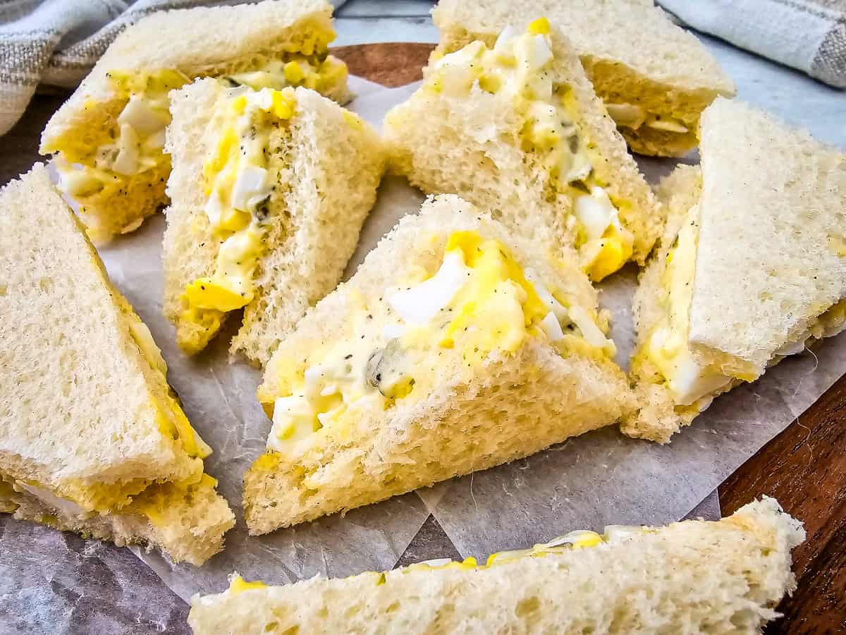 Close-up of egg salad tea sandwiches cut into triangles with creamy egg and dill mixture on white bread.