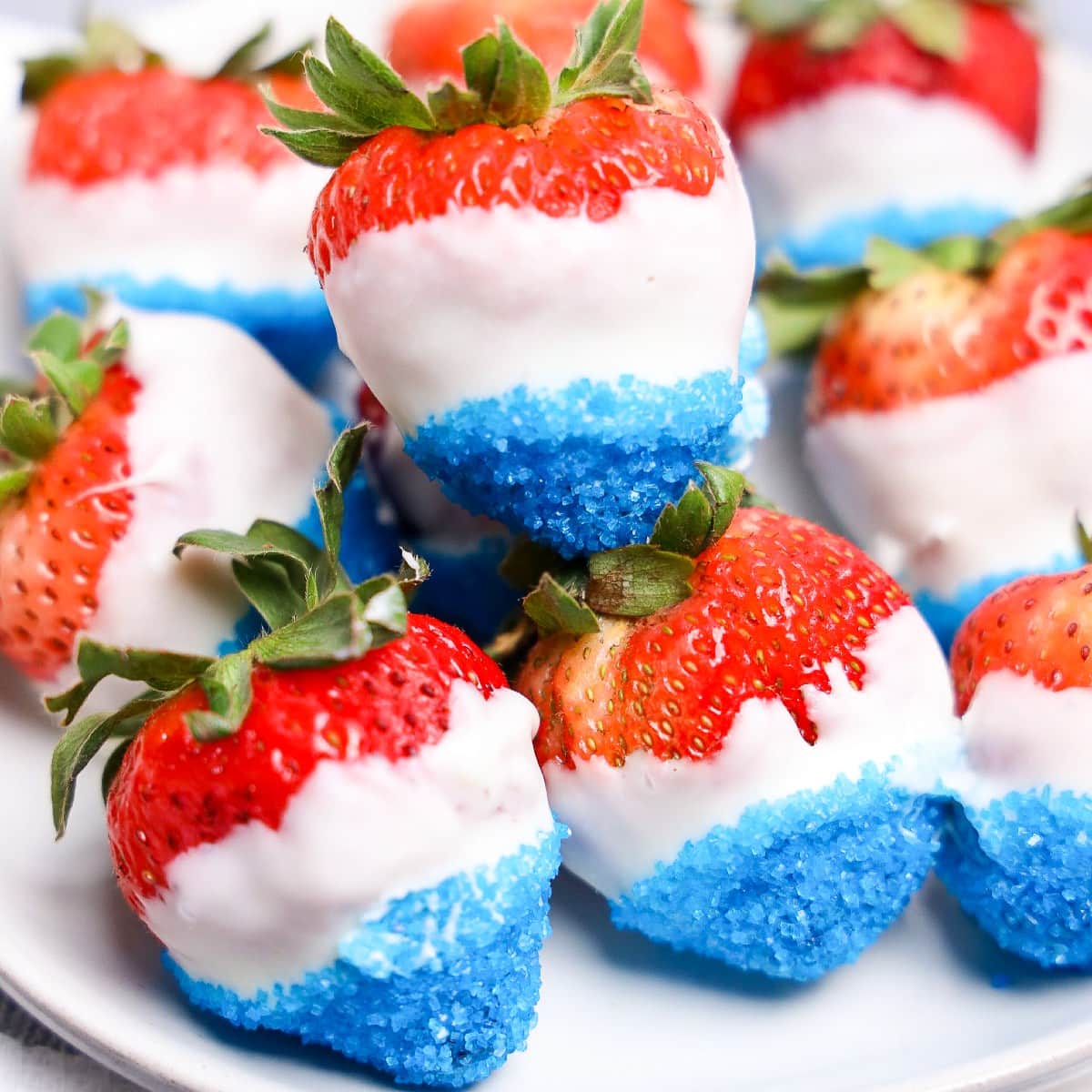 July 4th strawberries dipped in white chocolate with blue sugar crystals on plate.