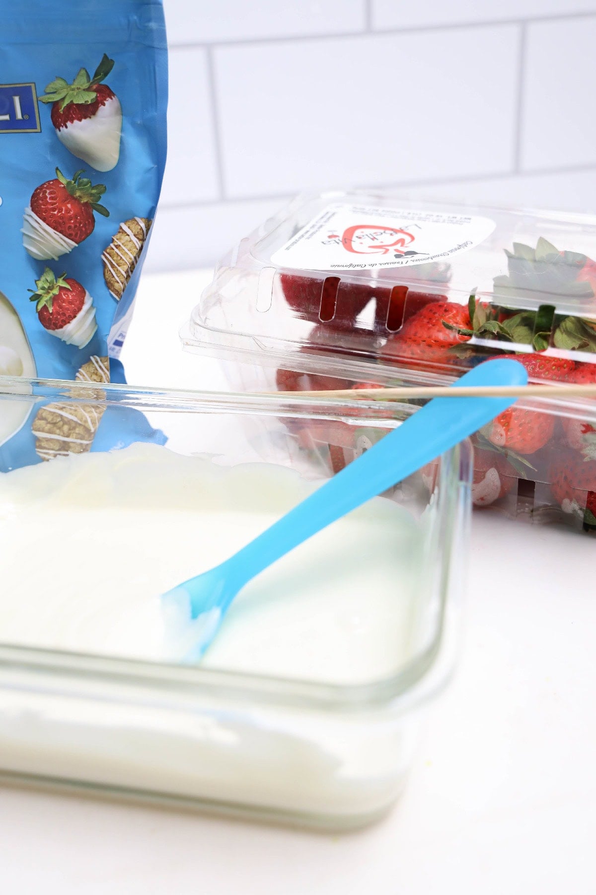 Melted white chocolate in glass dish with fresh strawberries ready for dipping.