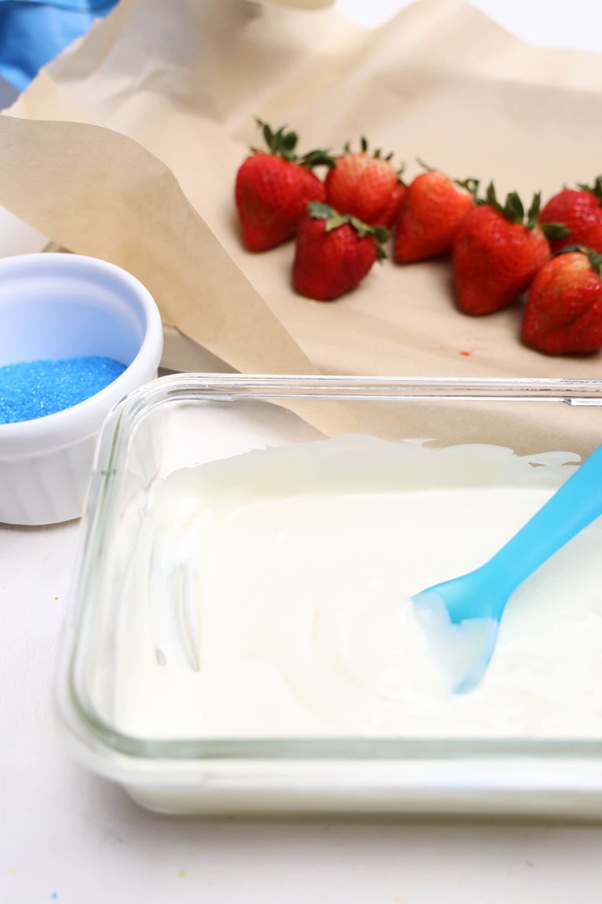 Fresh strawberries on parchment paper with blue sanding sugar and melted white chocolate.