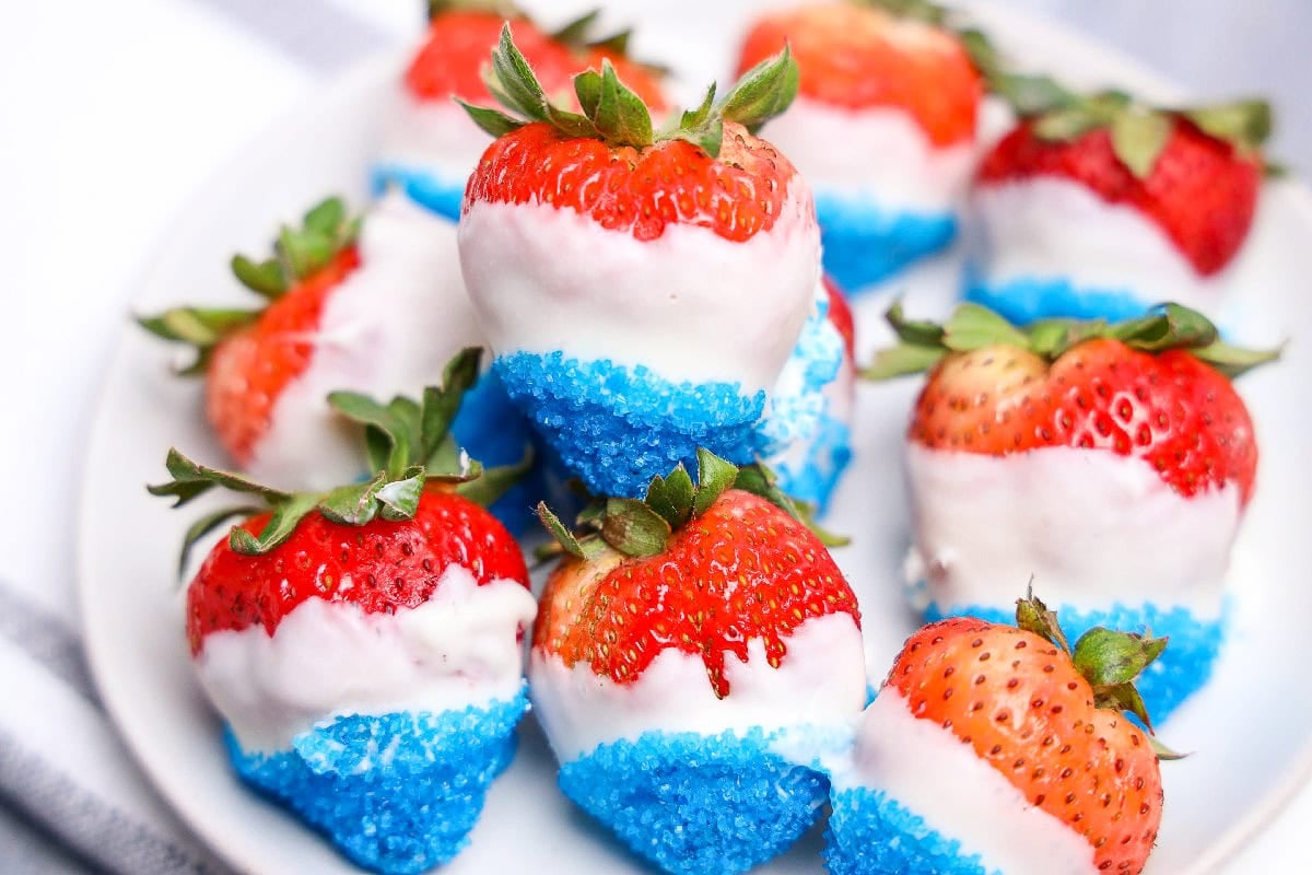 July 4th strawberries dipped in chocolate with blue sugar crystals on white plate.