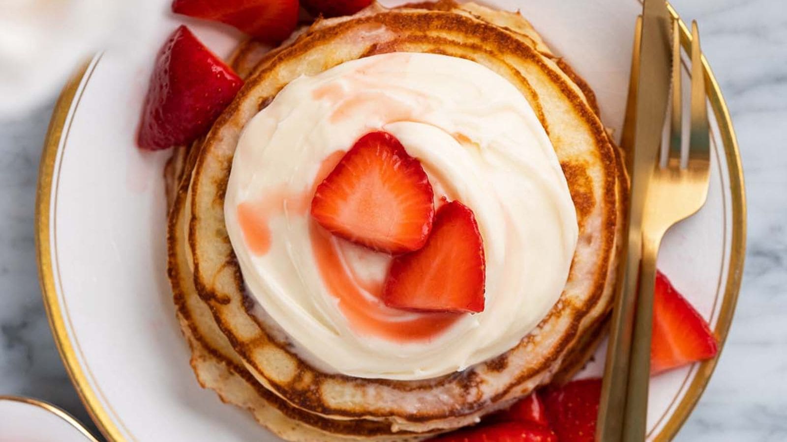 Strawberry cheesecake pancakes topped with berries and creamy cheesecake-style filling.