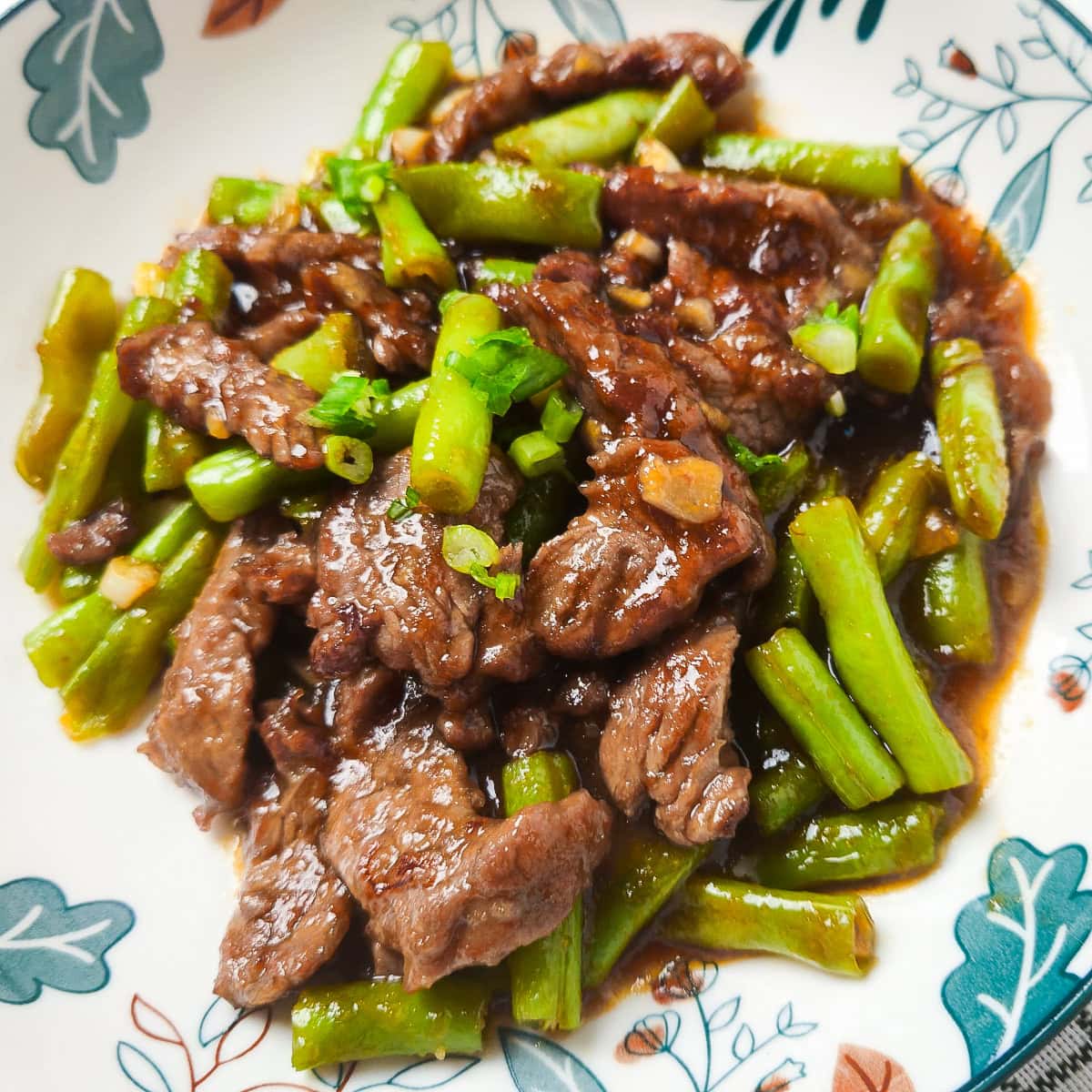 Beef and green beans stir fry in savory garlic sauce with tender sliced beef and crisp green beans, garnished with chopped scallions in a bowl.