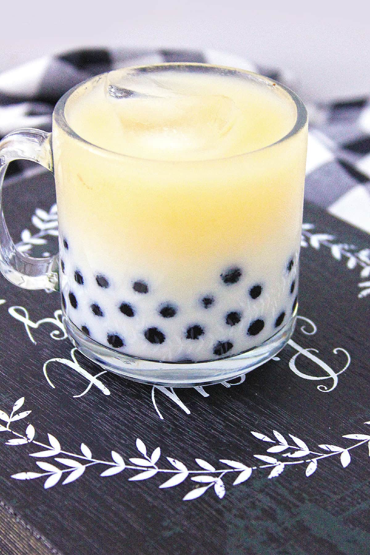 Creamy milk tea with black tapioca pearls in a clear glass cup.