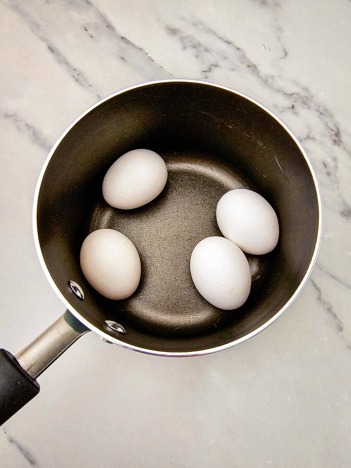 Eggs in a saucepan ready to be boiled for egg salad tea sandwiches on a marble countertop.