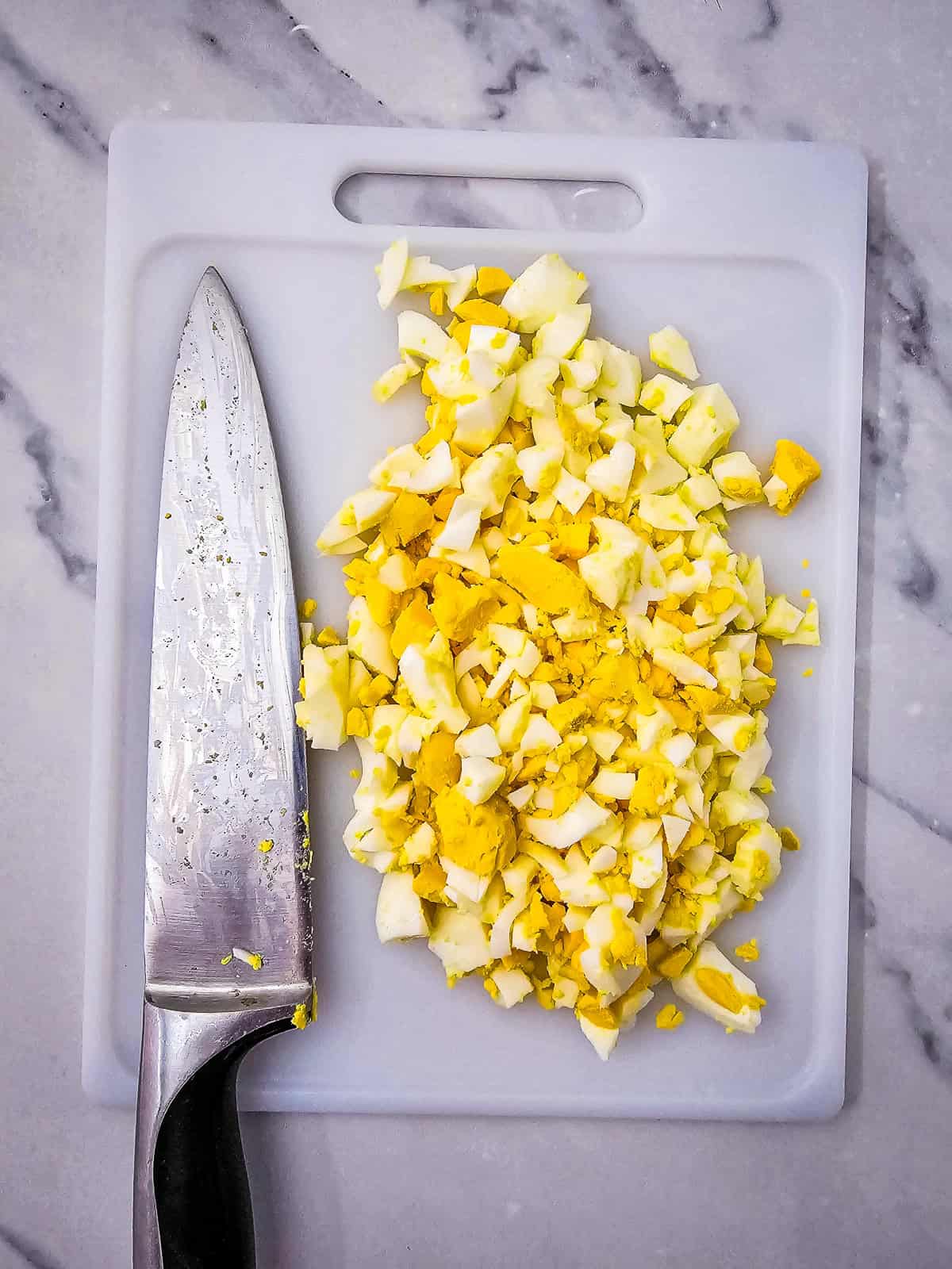 Finely chopped dill pickles on a white cutting board with a chef’s knife.